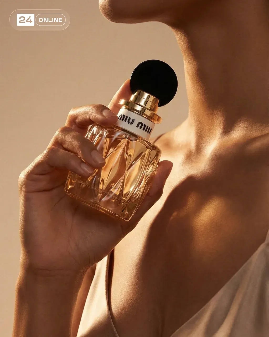 PRODUCT held gracefully near a model’s collarbone, bottle tilted slightly