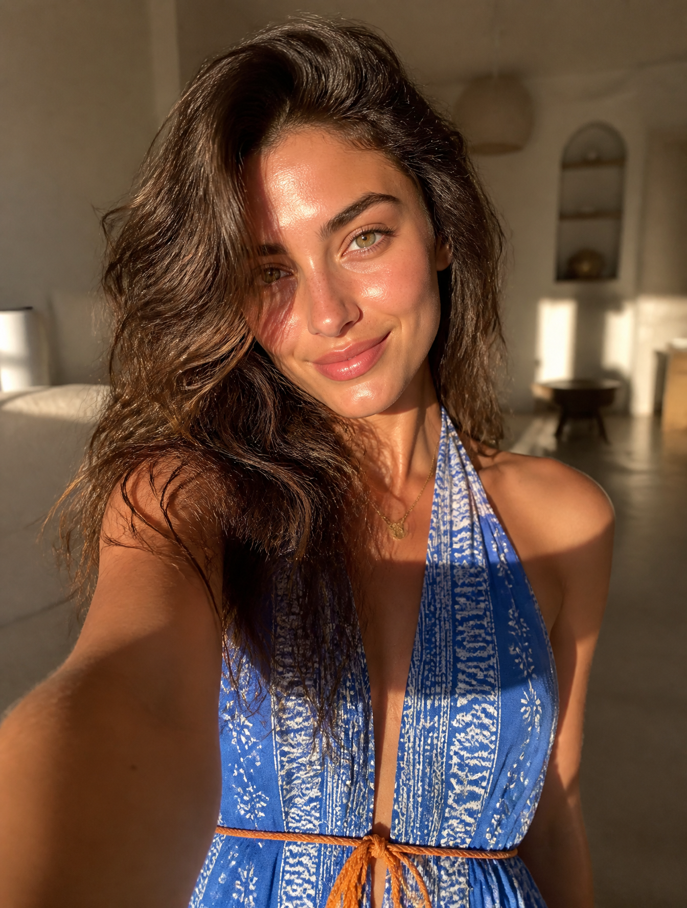 A young woman with voluminous, tousled brunette hair takes a selfie, her face illuminated…