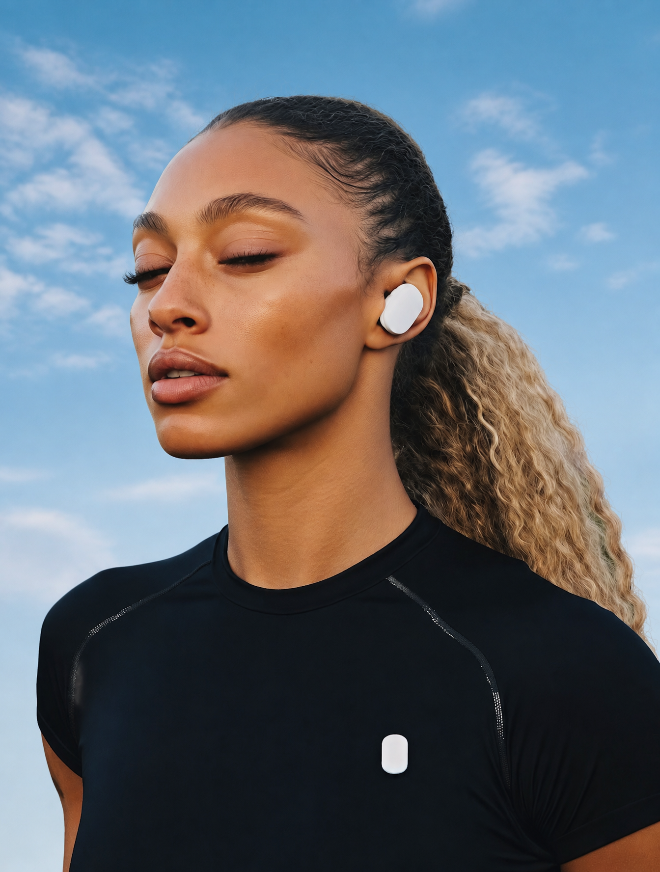 Confident woman with wireless earbuds in a blueish sky background, wearing a black athlet…