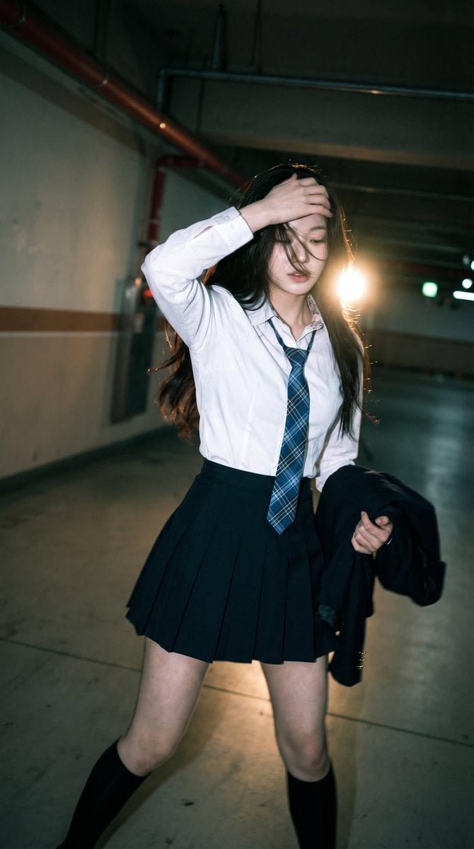 Candid portrait of a young woman in a dim parking garage, wearing a white shirt with a bl…