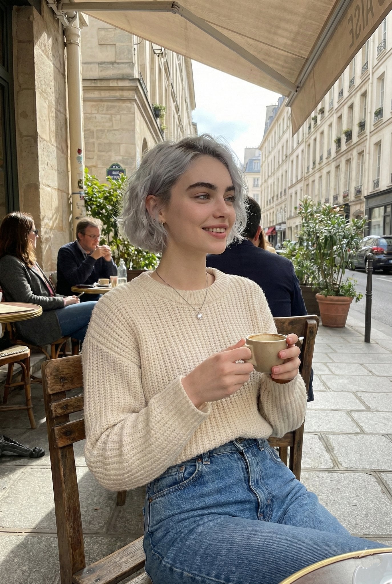 A candid lifestyle portrait of a young woman sitting at an outdoor Parisian café, holding…